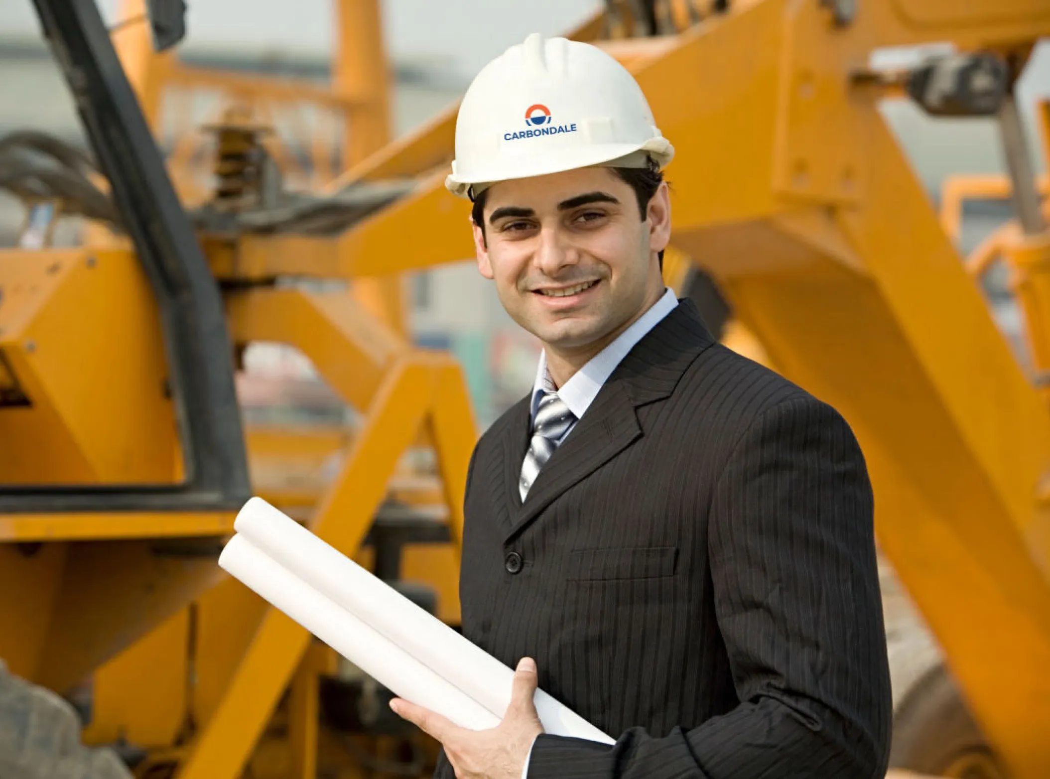 a_man_in_a_suit_and_hard_hat_holds_rolled_up_blueprints